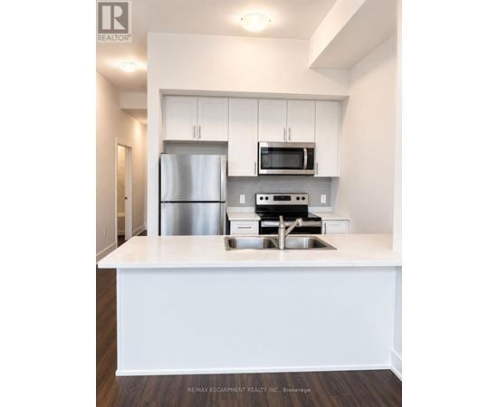 A white kitchen with a stainless steel refrigerator and microwave above the stove.