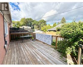 A wooden deck with a table and chairs is surrounded by greenery.