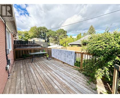 A wooden deck with a table and chairs is surrounded by greenery.