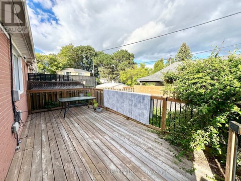A wooden deck with a table and chairs is surrounded by greenery.