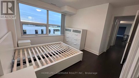 A room with a bed, dresser, and window with a view of buildings outside.