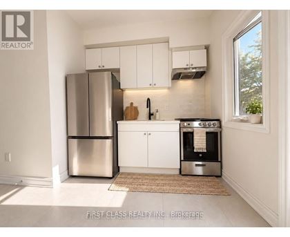 A kitchen with a stainless steel refrigerator and oven, white cabinets, and a window letting in natural light.