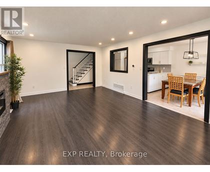 A spacious room with wooden flooring and a dining area in the background.