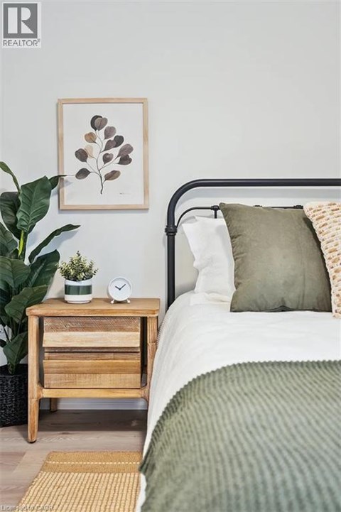 A bedroom with a bed, a nightstand with a plant, and a framed picture on the wall.