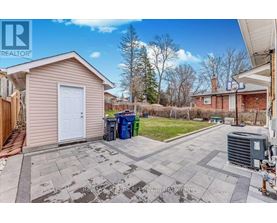 A small house with a white door is surrounded by a driveway and a green trash can.