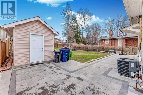 A small house with a white door is surrounded by a driveway and a green trash can.