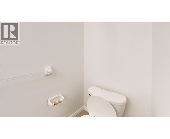 A white toilet in a bathroom with a roll of toilet paper on the wall.