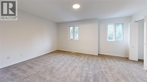 A spacious room with a carpeted floor and two windows.