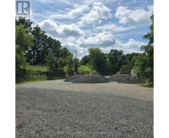 A gravel road leads to a pile of gravel surrounded by trees.