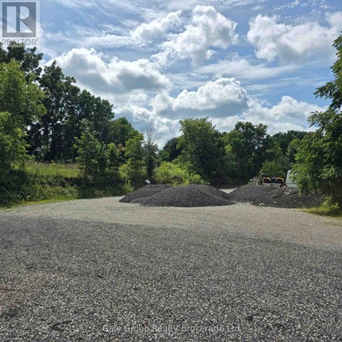 A gravel road leads to a pile of gravel surrounded by trees.