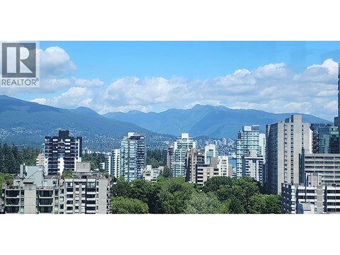 A cityscape with buildings and trees in the foreground and mountains in the background.
