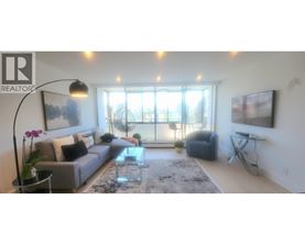 A living room with a grey couch, a glass table, and a large window.