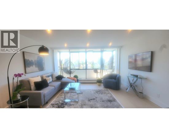 A living room with a grey couch, a glass table, and a large window.