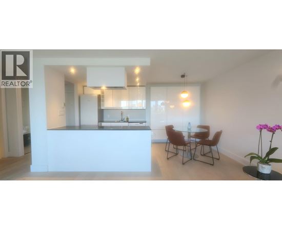 A realtor logo is on the wall of a modern kitchen and dining area.