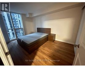 A bedroom with a bed, wooden floors, and a window overlooking a city.
