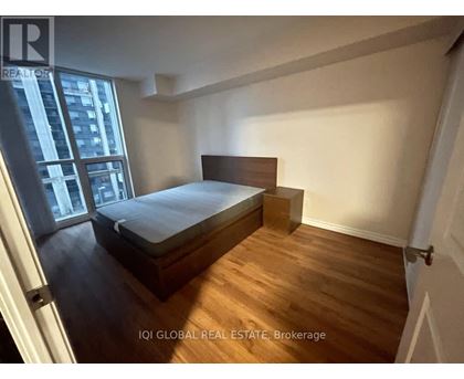 A bedroom with a bed, wooden floors, and a window overlooking a city.