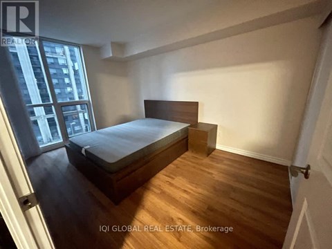 A bedroom with a bed, wooden floors, and a window overlooking a city.