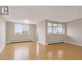 A spacious room with wooden flooring and large windows overlooking a cityscape.