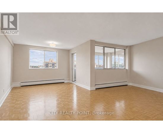 A spacious room with wooden flooring and large windows overlooking a cityscape.