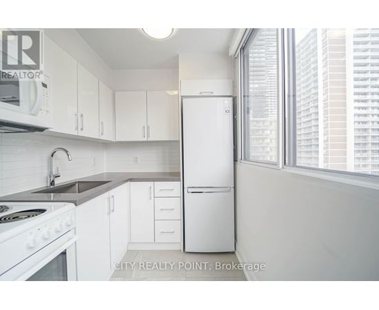 A white refrigerator is in a kitchen with white cabinets.