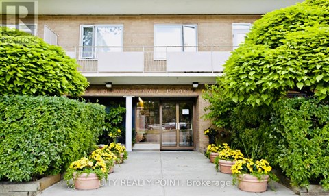 A building entrance with a glass door and windows, flanked by two large bushes.