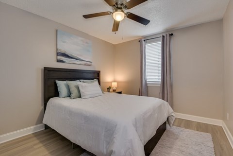 A bedroom with a bed, pillows, a ceiling fan, and a painting on the wall.