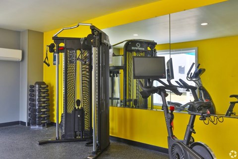 A gym with a yellow wall and a treadmill and exercise bike.