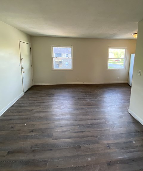 A room with wooden flooring and two windows.
