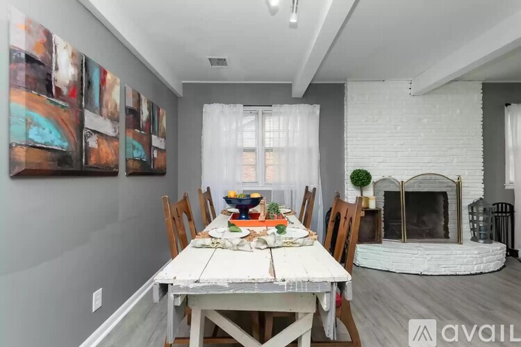 A dining room with a white table and chairs, a fireplace, and a painting on the wall.