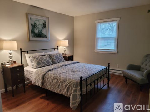 A bedroom with a bed, two lamps, a chair, and a painting on the wall.