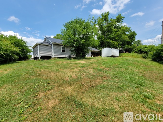 A grassy field with a house and a shed in the background.