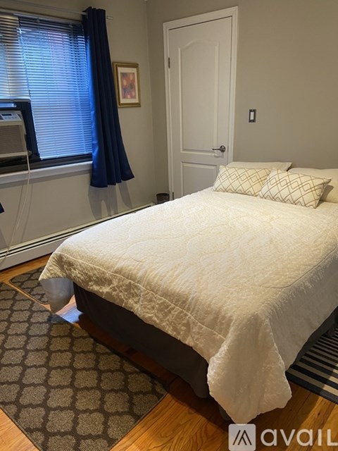 A bedroom with a bed, a window with blinds, a door, and a rug on the floor.