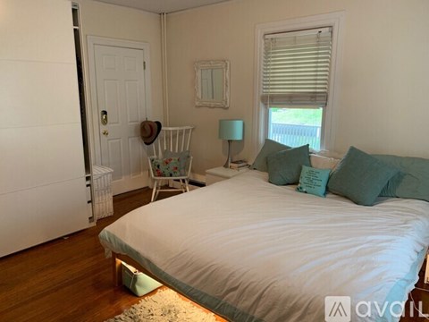 A bedroom with a white bed and a window with blinds.