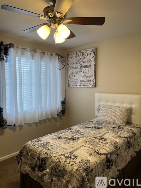 A bedroom with a bed, a ceiling fan, and a framed picture on the wall.