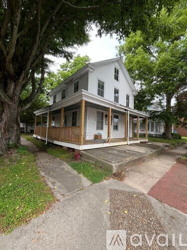 A white house with a porch and a tree in front.