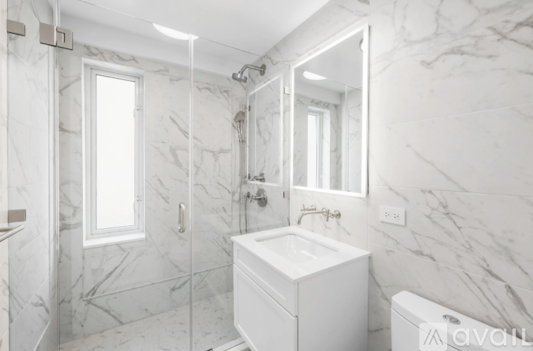 A white bathroom with marble tiles and a large mirror.
