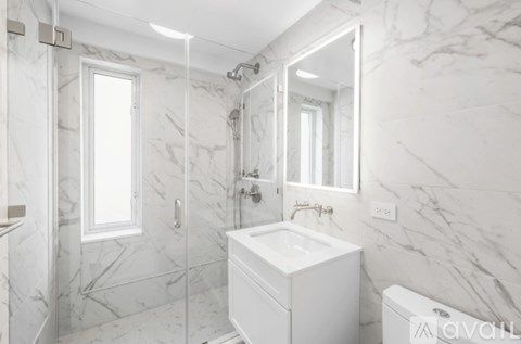 A white bathroom with marble tiles and a large mirror.