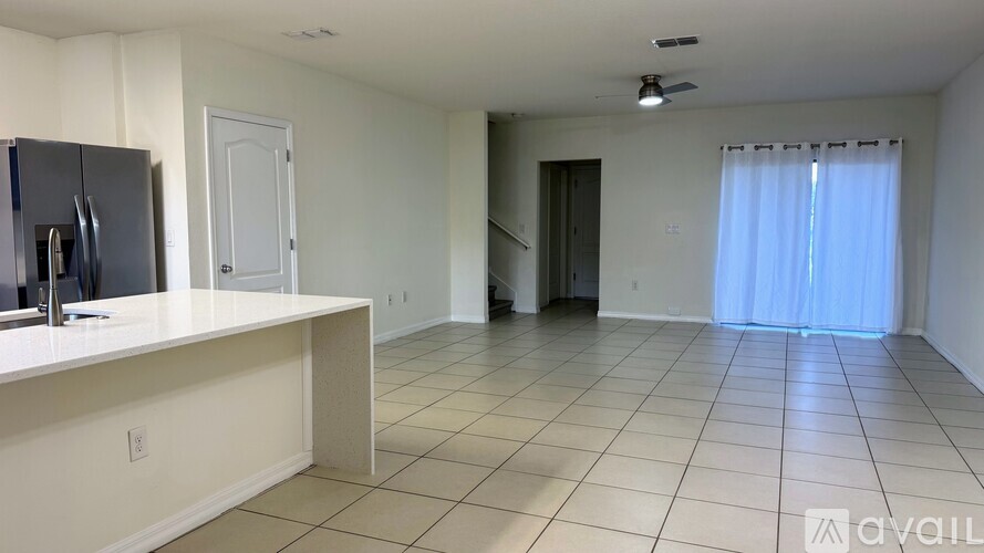 A spacious room with a kitchenette and a window with curtains.