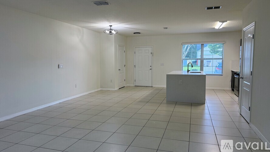 A spacious room with white walls and tile flooring, featuring a kitchenette with a sink and stove.
