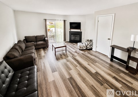 A living room with a black leather couch and a wooden floor.