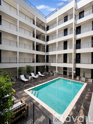 A swimming pool is surrounded by lounge chairs in a courtyard.
