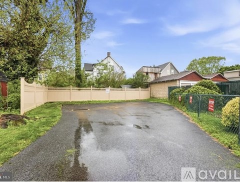 A wet driveway leads to a gated property with a white house in the background.