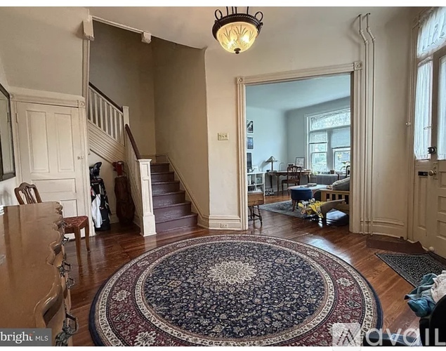 A large, open living room with a staircase and a rug in the center.