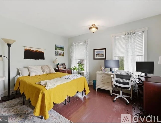 A bedroom with a bed covered in a yellow bedspread and a desk with a computer.