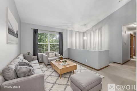 A living room with a grey couch, a coffee table, and a large window with curtains.