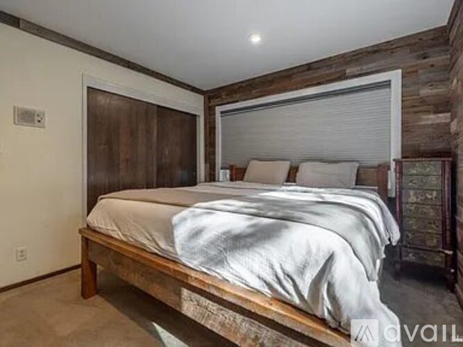 A bedroom with a bed, wooden headboard, and a window with blinds.