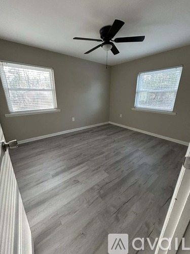 A room with a ceiling fan and two windows.