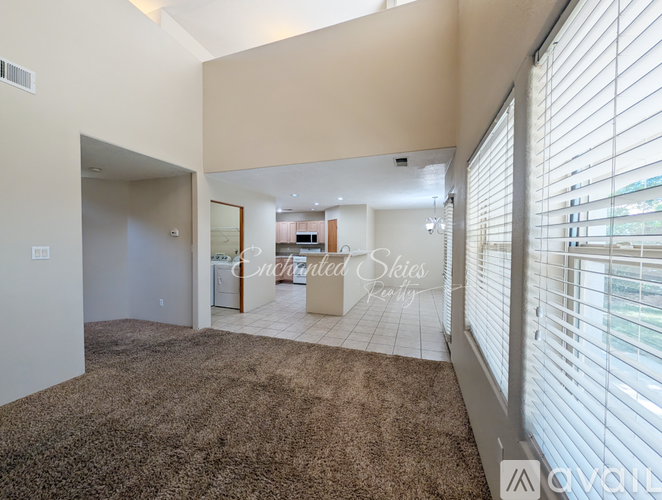 A living room with a brown carpet and a large window with blinds.
