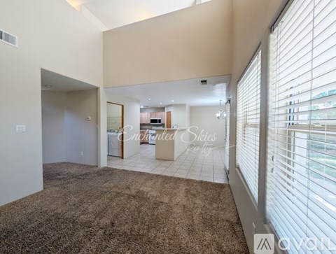 A living room with a brown carpet and a large window with blinds.