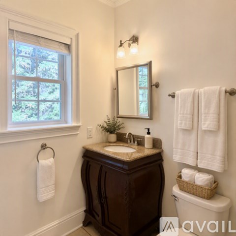 A bathroom with a brown vanity, a towel rack with two white towels, and a window with a view of trees.
